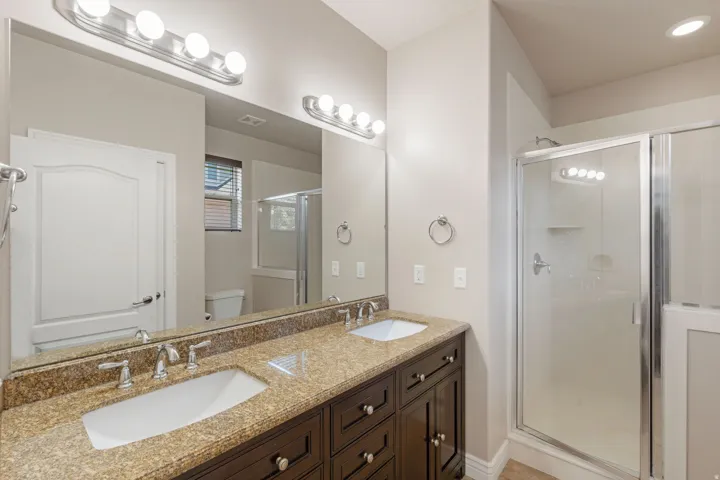 Dual vanity with integrated sinks, granite-finish countertop, dark wood-finish cabinetry, and a glass-enclosed shower