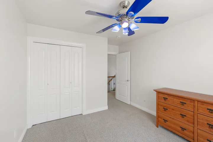 Light gray wall paint, carpeting, bi-fold closet doors, and a ceiling fan with light fixture
