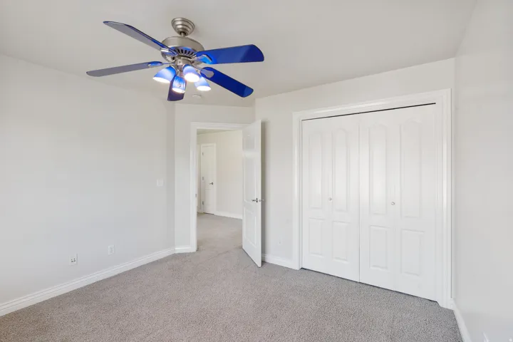 Neutral wall color, light gray carpeting, bi-fold closet doors, and overhead lighting with fan