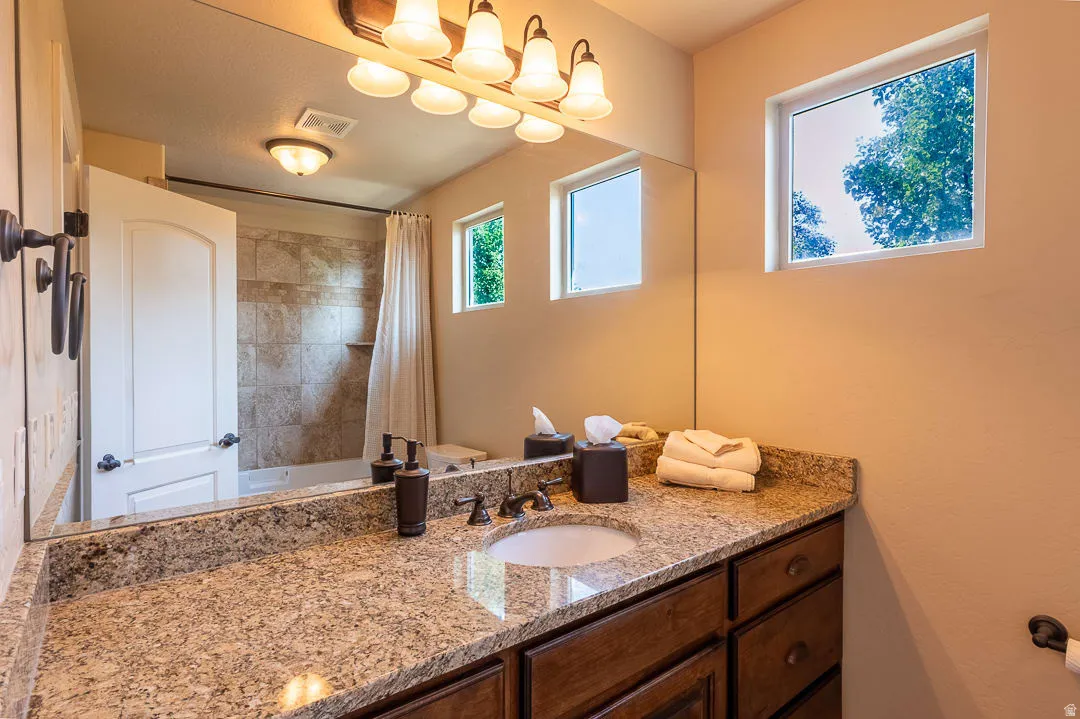 Granite-style countertop with an undermount sink, rich wood-finish cabinetry, and a full-width mirror