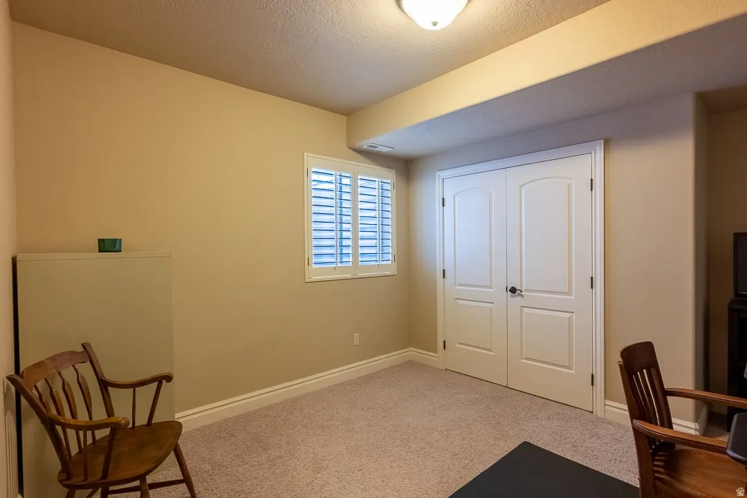 Carpeted room with a window featuring white plantation shutters, white paneled double doors, and a ceiling-mounted light fixture
