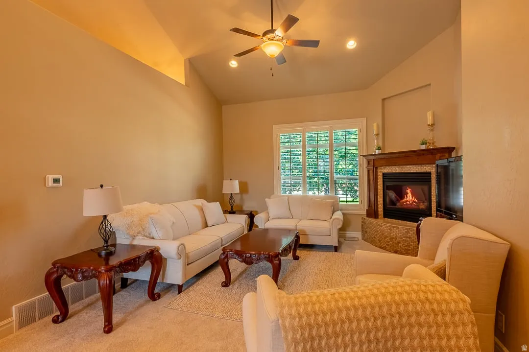 Vaulted ceiling with a ceiling fan, fireplace with a wood-mantel, mosaic tile surround, and stone hearth, and window with plantation shutters