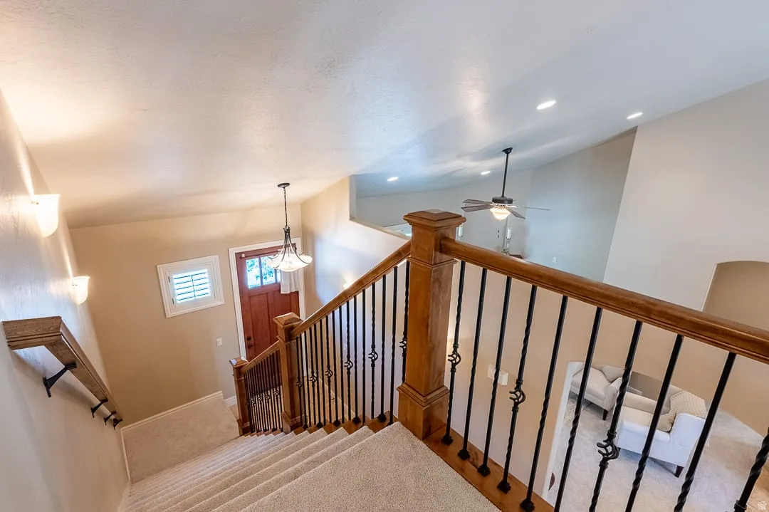 Carpeted staircase with wrought iron and wood balusters, wood handrail, and wall sconces