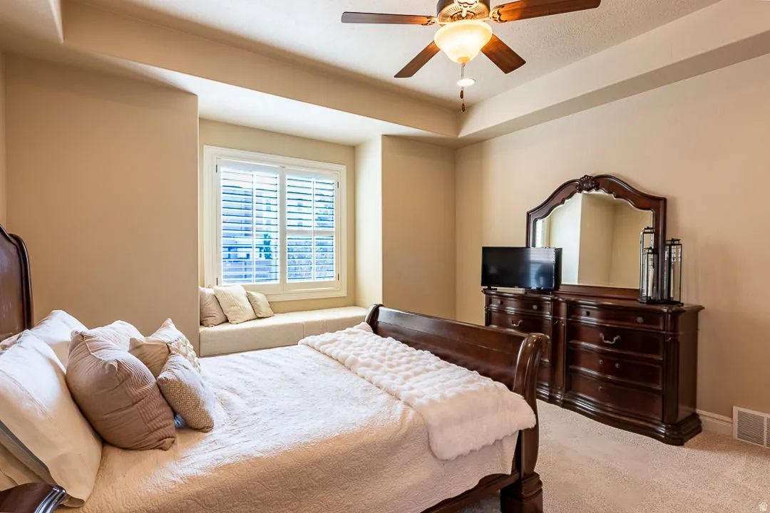 Window seating with plantation shutters, ceiling fan, tray ceiling, and carpeted flooring
