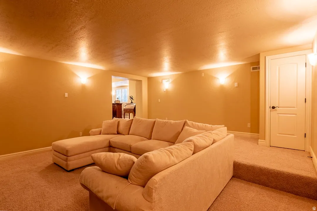 Carpeted living space with recessed lighting and sconces, featuring a paneled interior door with dark hardware, and an archway leading to an adjacent area