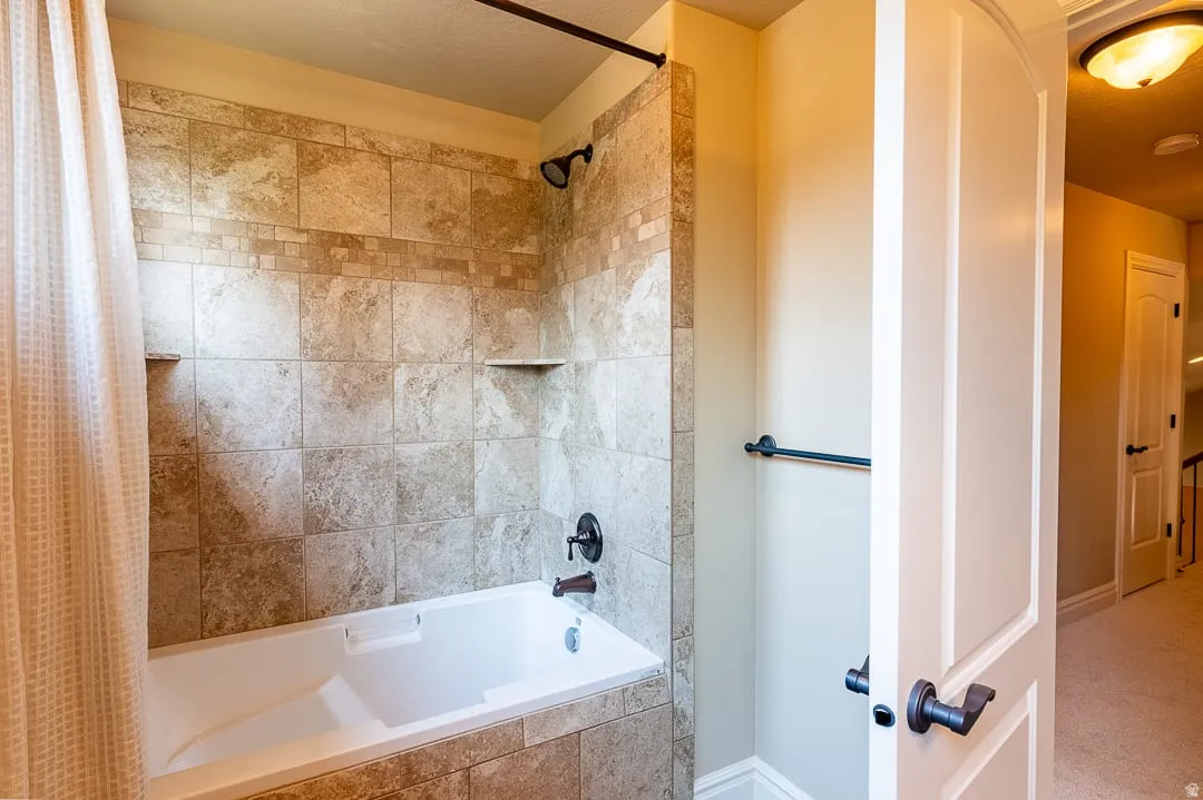 Bathtub with a tiled surround, recessed shelving, and dark bronze fixtures