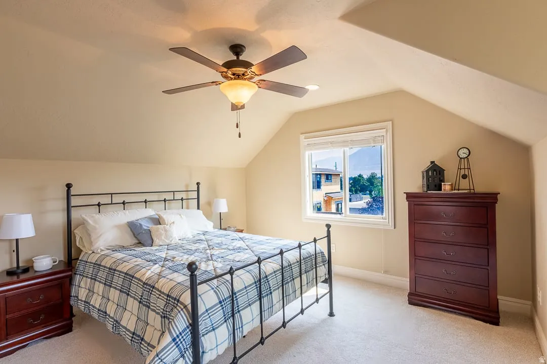 Ceiling fan with integrated lighting, a double-hung window, sloped ceilings, and wall-to-wall carpeting