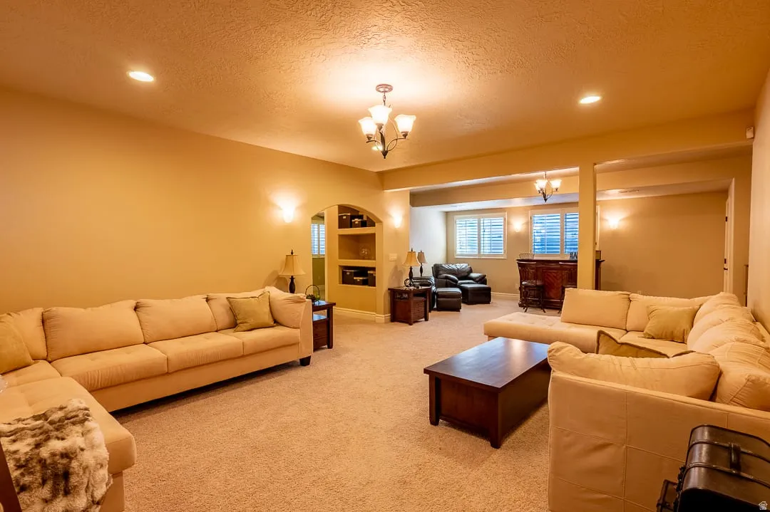 Recessed lighting, wall sconces, ceiling-mounted chandelier, arched built-in shelving, and carpeted flooring