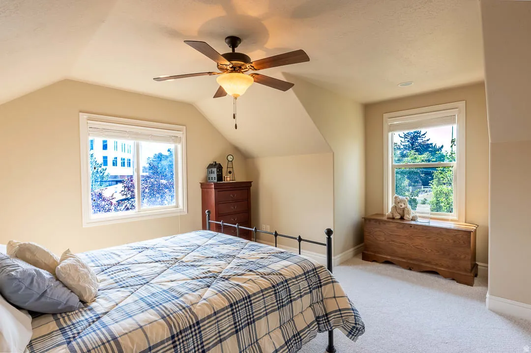Sloped ceilings with a ceiling fan, dual windows, and light-colored wall finishes