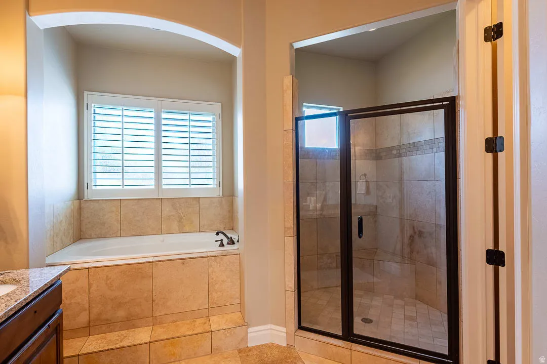 Built-in corner tub with tiled surround, plantation shutters, and an adjacent walk-in shower with clear glass enclosure and tiled walls