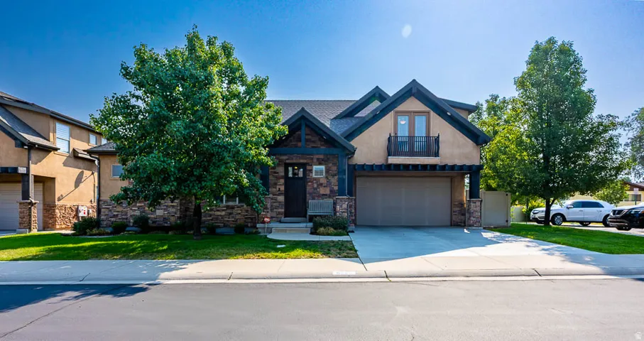 Stucco and stone exterior with architectural trim, a prominent attached two-car garage, and a second-story balcony