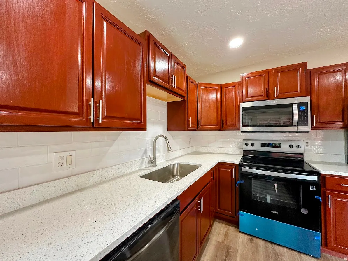 Kitchen featuring rich wood-finish cabinetry, white subway tile backsplash, white speckled countertops, and stainless steel appliances