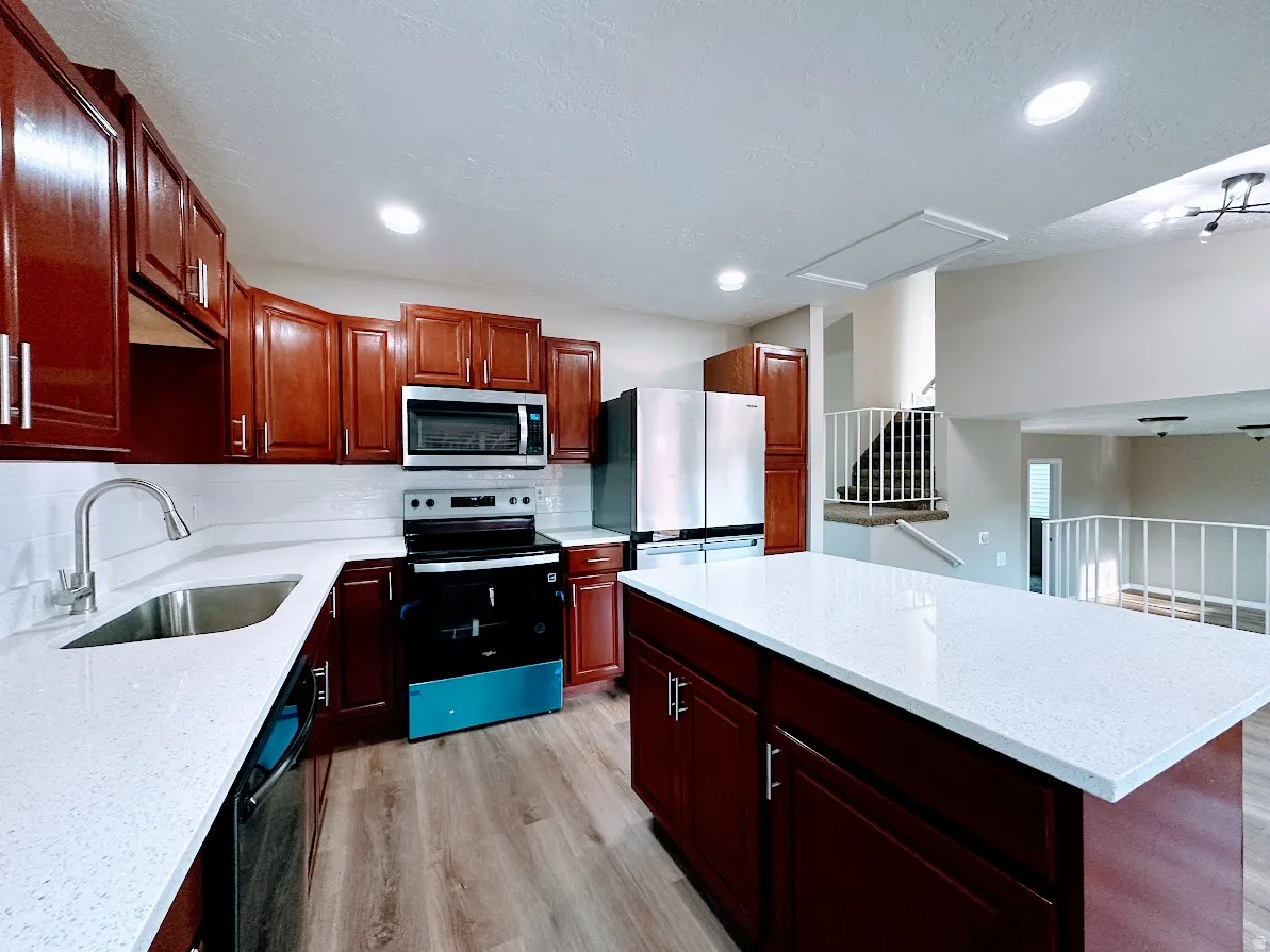 Kitchen featuring wood-finish cabinetry with stainless steel hardware, white quartz countertops, stainless steel appliances, and wood-finish flooring