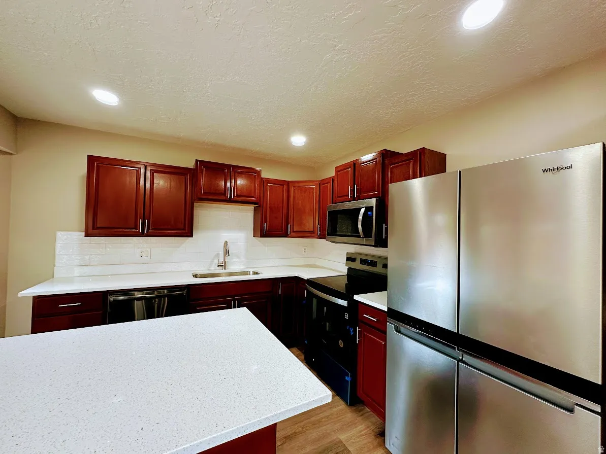 Kitchen featuring wood-finish cabinetry, white countertops, a subway tile backsplash, and stainless steel appliances