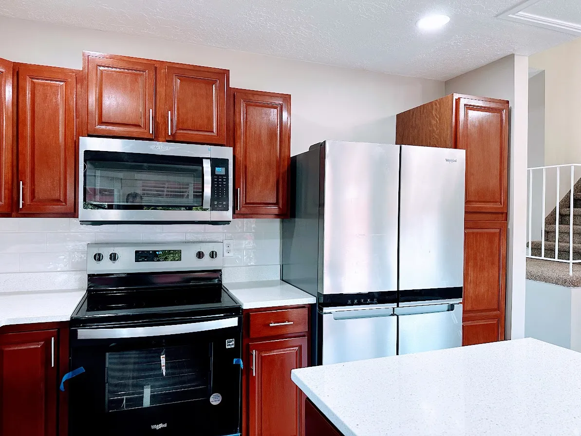Kitchen featuring wood-finish cabinetry, white tile backsplash, stainless steel appliances, and white speckled countertops