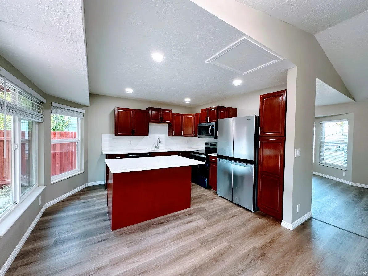 Kitchen featuring cherry wood-finish cabinetry, stainless steel appliances, a central island with a white countertop, and wood-finish flooring