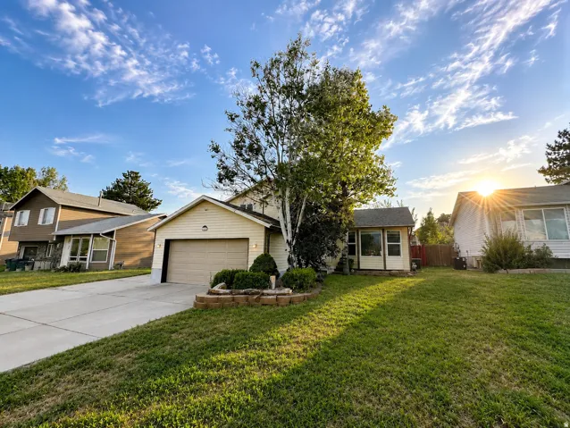 Exterior featuring horizontal siding, an attached garage, a paved driveway, a mature tree, and a grass lawn