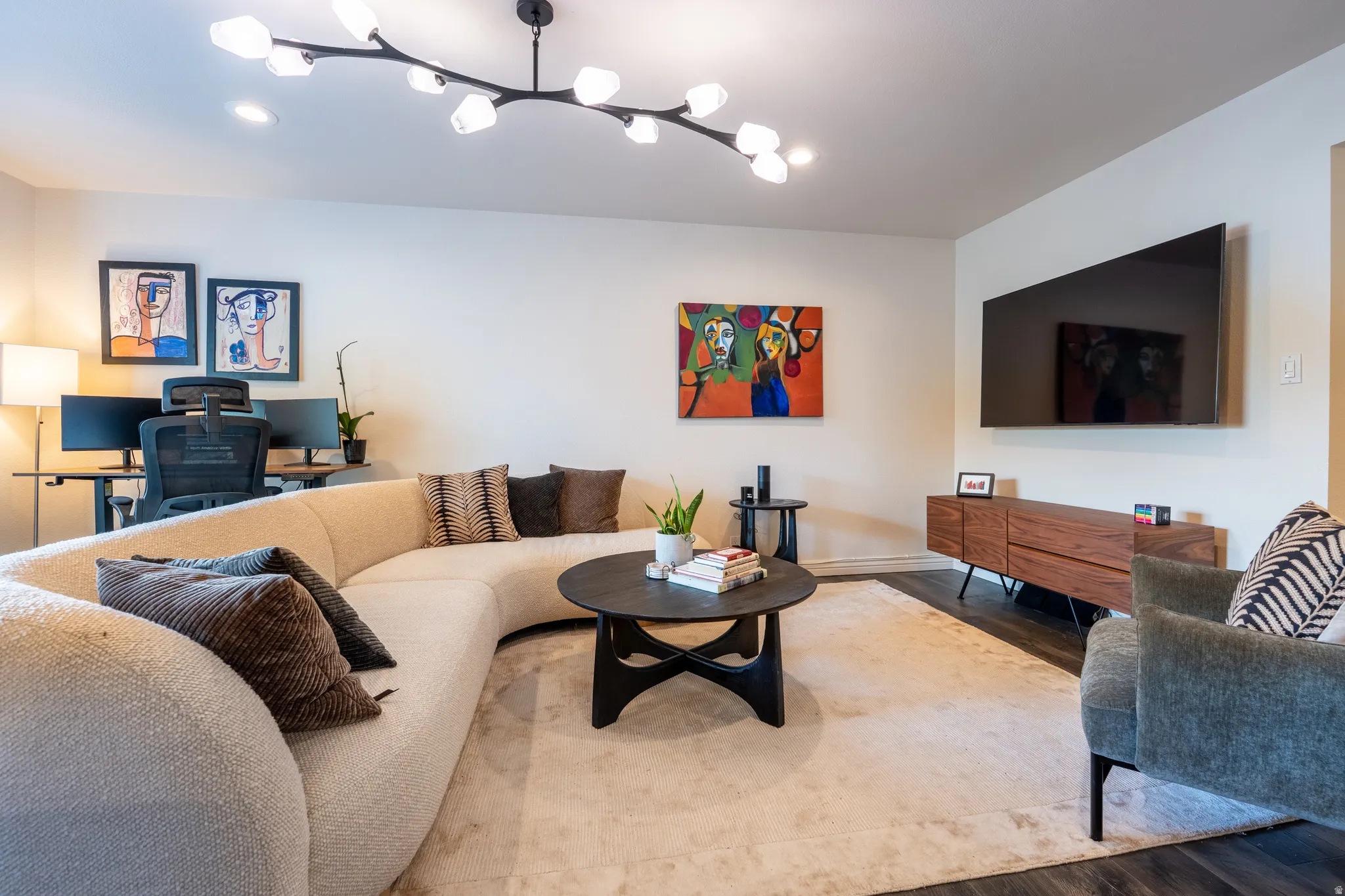 Hardwood-style flooring with a light-toned area rug, a contemporary multi-bulb ceiling fixture, a wall-mounted flat-screen display, and a modern wood media console