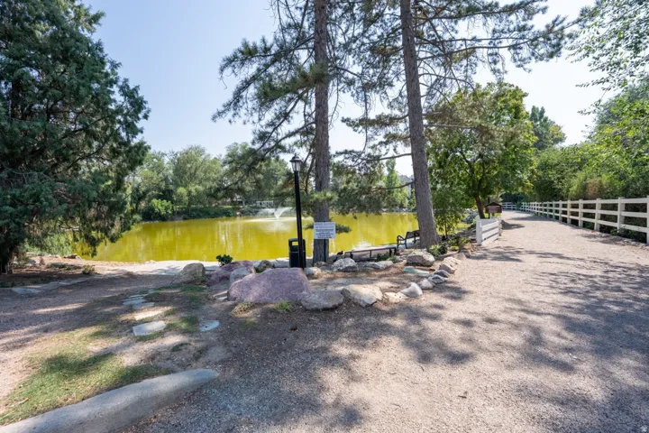 Pond with fountain feature, mature trees, gravel pathway, white fencing, and stone accents