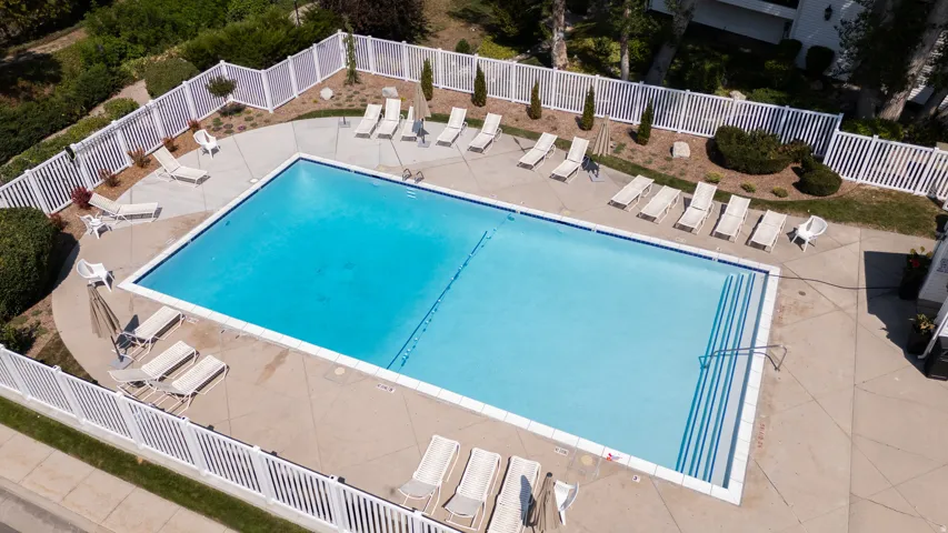 Rectangular swimming pool with integrated steps, surrounded by a concrete deck, white privacy fencing, and landscaped perimeter