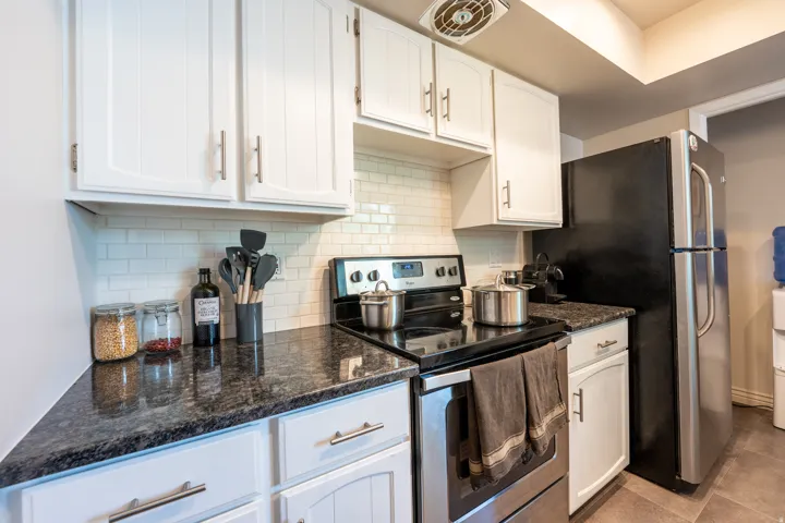 White shaker-style cabinetry, dark speckled countertops, subway tile backsplash, stainless steel range, and a stainless steel refrigerator