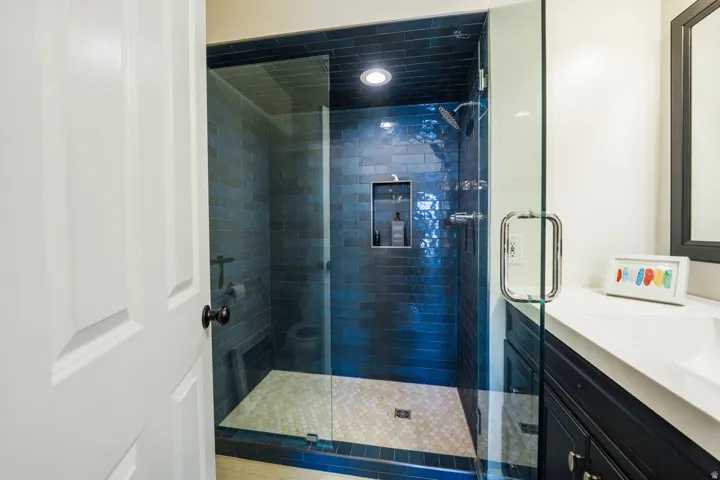 Walk-in shower with dark blue subway tile, recessed niche, and glass enclosure