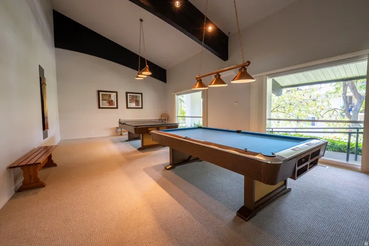 Spacious room with vaulted ceilings, exposed dark beams, wall-to-wall carpeting, and large windows