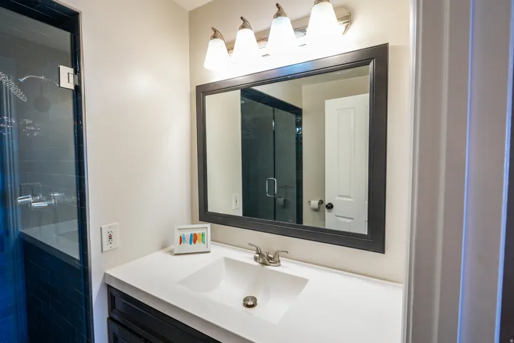 Bathroom featuring a framed mirror, vanity with an integrated sink, brushed nickel faucet, and a glass-enclosed shower with subway tile