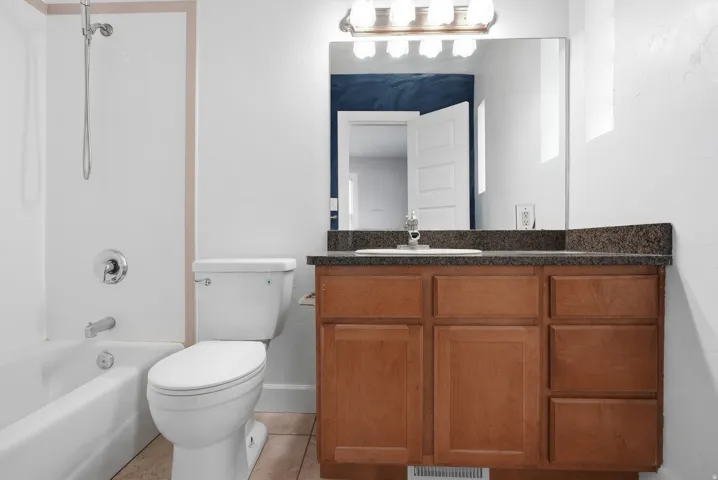 Bathroom with a white bathtub, toilet, and a vanity featuring wood-finish cabinetry and a stone-look countertop
