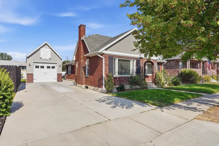 Brick exterior with a prominent chimney, concrete driveway, and a detached two-car garage featuring a barn-style door