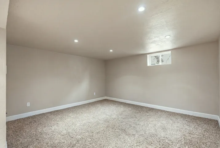 Recessed lighting, neutral-toned walls, plush carpeting, white trim, and a high window