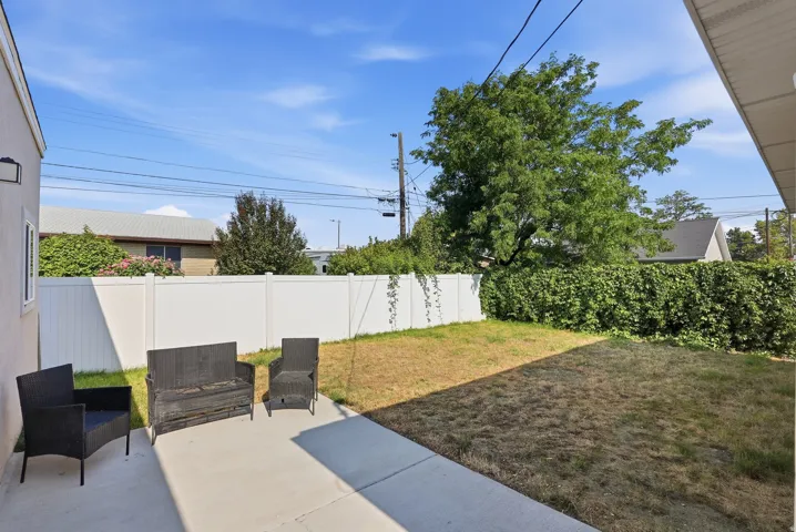 Paved patio with an exterior wall lantern, a white privacy fence, and mature perimeter hedging