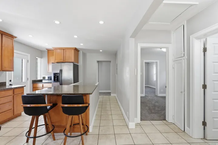 Kitchen featuring wood cabinetry, stainless steel refrigerator, and a breakfast bar with stone-finish countertop