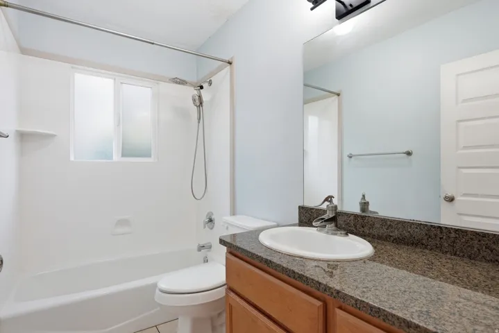 Bathroom featuring a white bathtub, a window with frosted glass, a vanity with a light wood-finish cabinet, and a dark speckled countertop