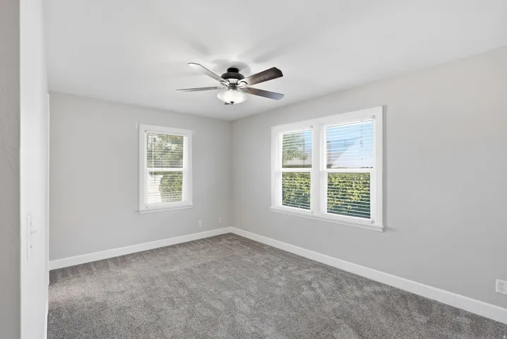 Neutral wall paint, ceiling fan with integrated lighting, two windows with blinds, and gray carpeting