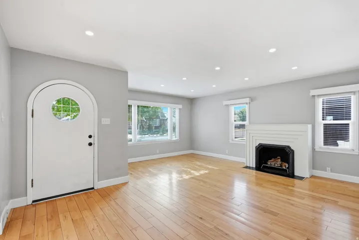 Hardwood flooring throughout, recessed lighting, arched entry door with circular glass insert, white fireplace with a dark surround, and multiple windows