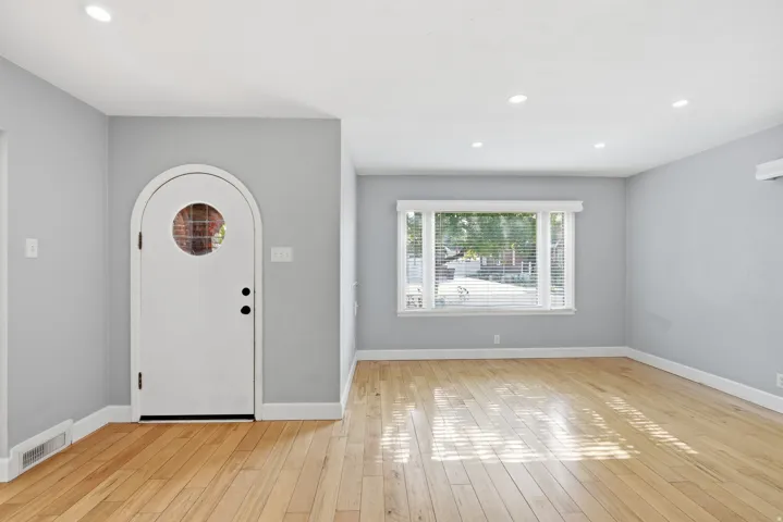 Light wood-finish flooring, recessed ceiling lighting, and an arched entry door with a circular glass inlay