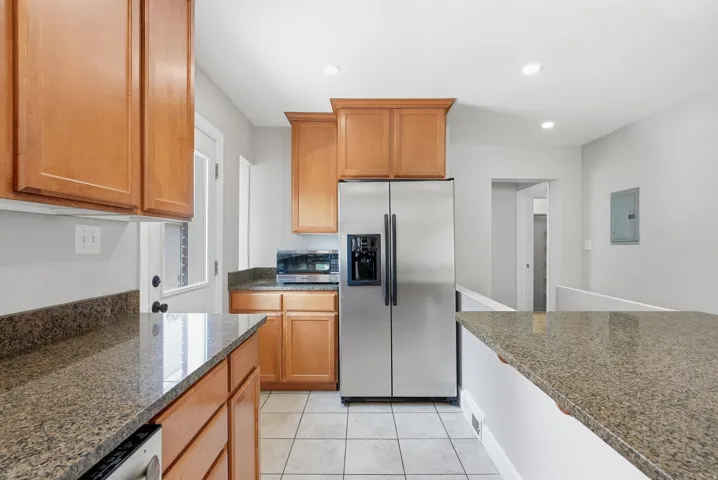 Kitchen featuring wood cabinetry, granite countertops, stainless steel refrigerator, tile flooring, and recessed lighting