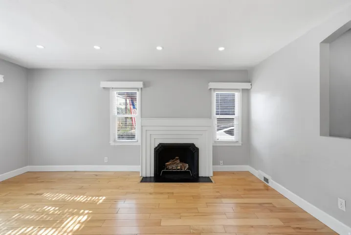 Recessed lighting, wood-finish flooring, white trim, and a fireplace with a dark-tone surround