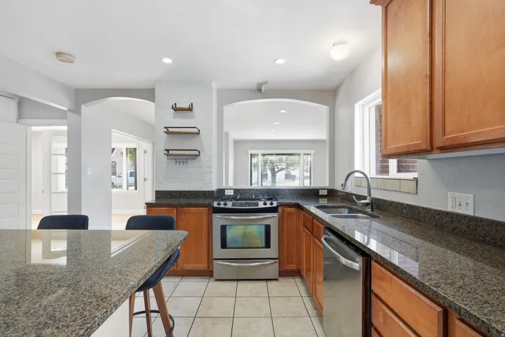 Kitchen featuring granite countertops, wood cabinetry, stainless steel appliances, and tile flooring