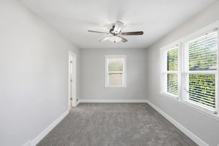 Carpeted room featuring multiple windows, a ceiling fan with integrated lighting, and a white interior door
