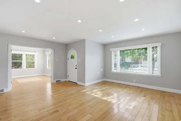 Bright, open living spaces showcase gleaming wood-finish flooring throughout, abundant natural light from multiple large windows with blinds, recessed ceiling lighting, and fresh gray-toned walls