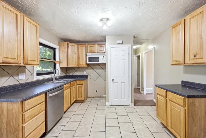 Kitchen featuring light wood-finish cabinetry, dark countertops, a stainless steel dishwasher, and a microwave