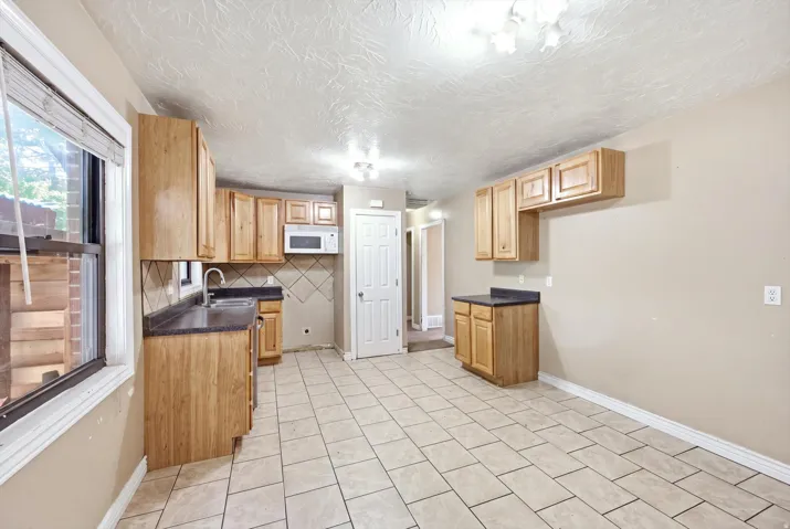 Kitchen featuring tile flooring, wood-finish cabinetry, dark countertops, a built-in microwave, and a single-basin sink