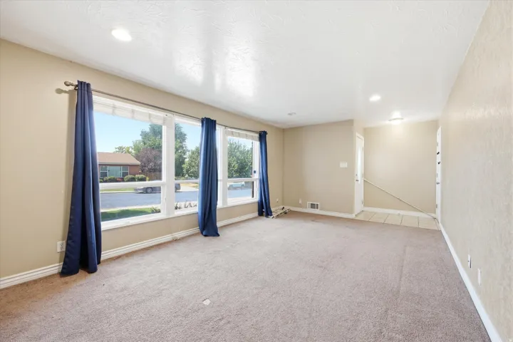 Expansive living area with large picture windows, recessed lighting, neutral tone walls, and soft carpet flooring