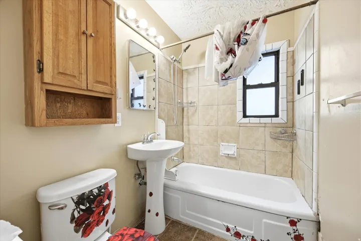 Pedestal sink, wall-mounted wood-finish cabinet, bathtub with shower fixture, and tiled shower surround