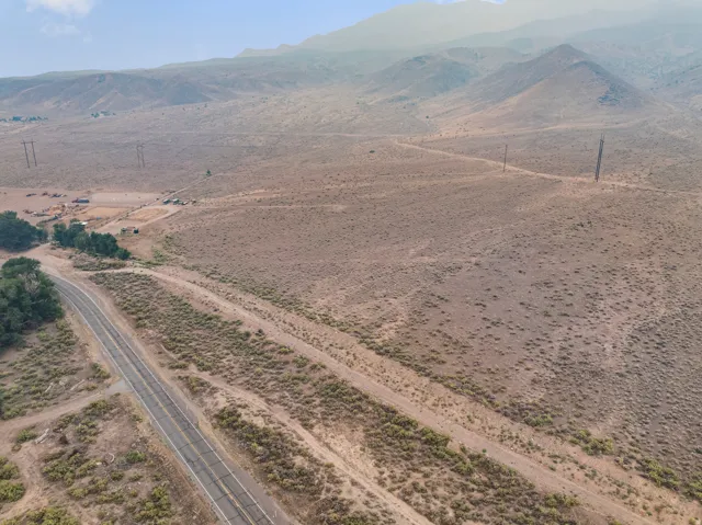 Expansive undeveloped land featuring a paved road, scattered vegetation, and distant mountains
