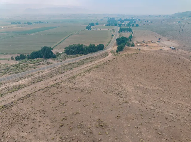 Expansive undeveloped land featuring natural desert vegetation, a road, and distant agricultural fields