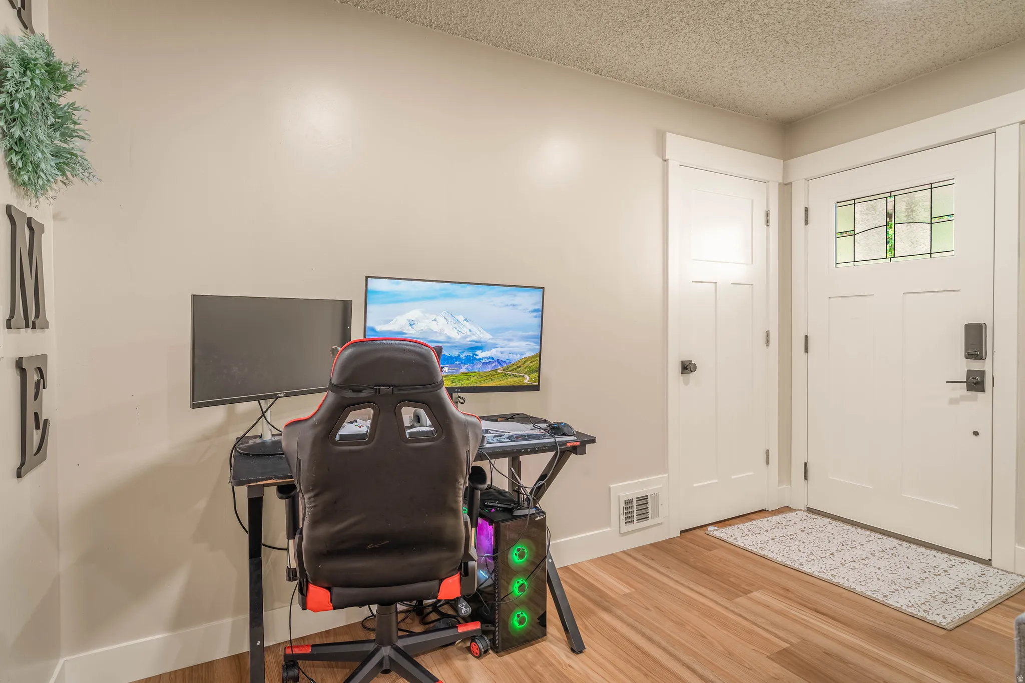 Dedicated home office featuring hardwood flooring, dual monitor setup with professional gaming chair, and abundant natural light from street-facing windows