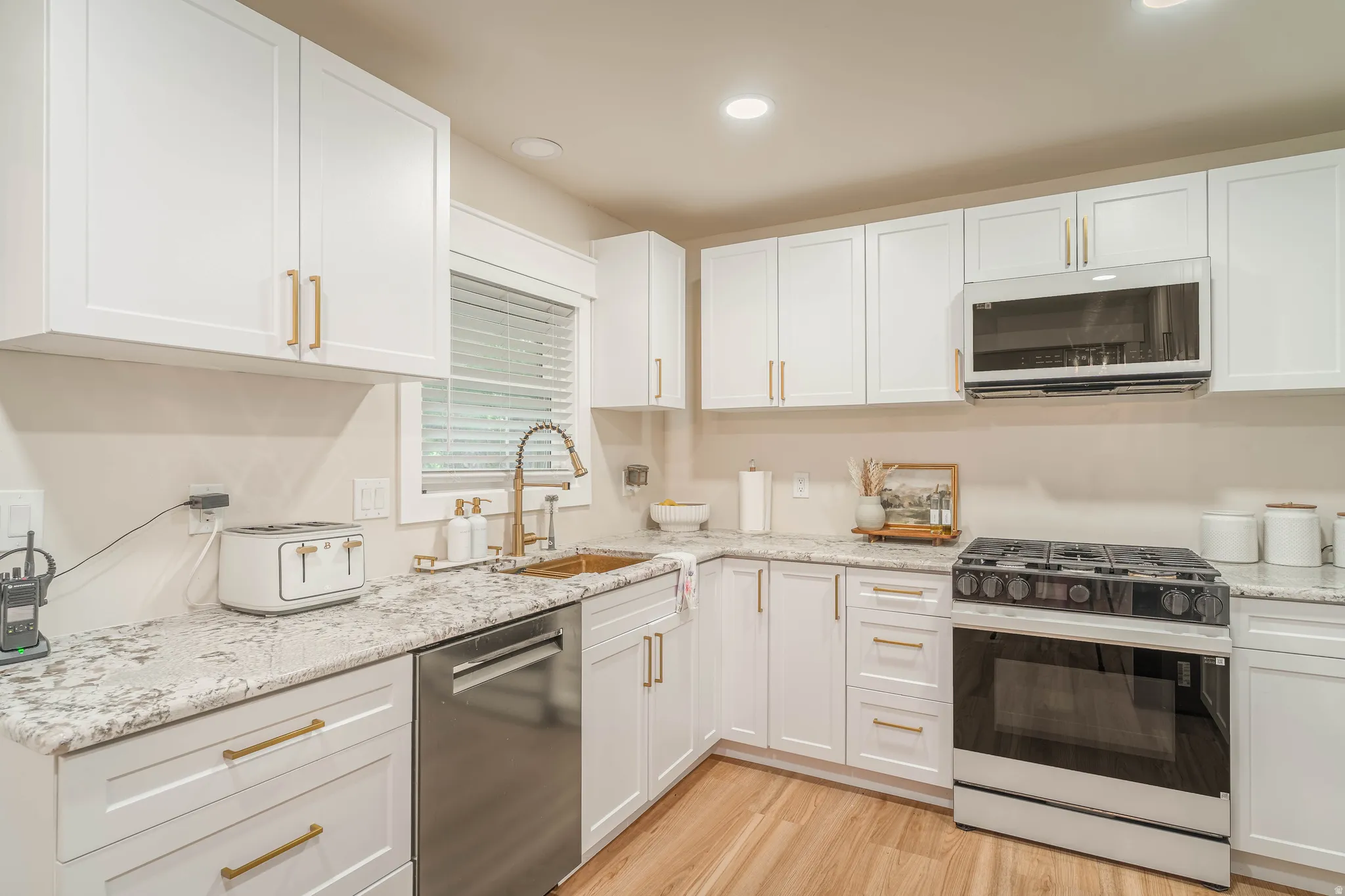 Modern kitchen featuring white shaker cabinetry, granite countertops, stainless steel appliances, wood-finish flooring, and a window with blinds
